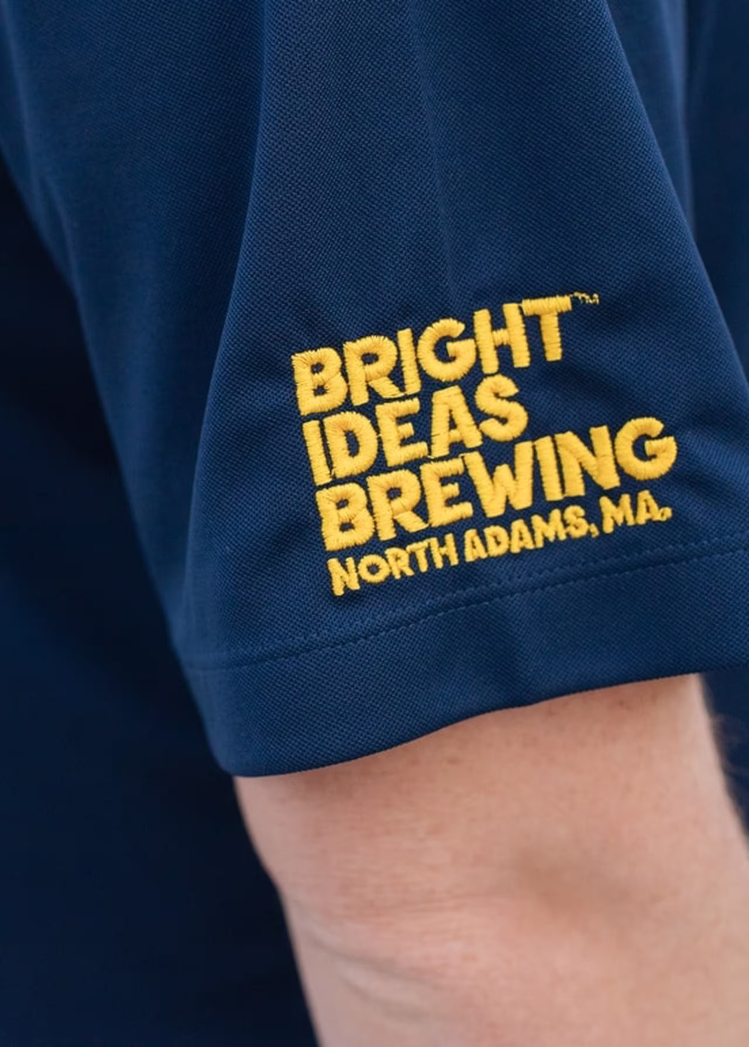 close-up on the sleeve of a polo that is embroidered with yellow text