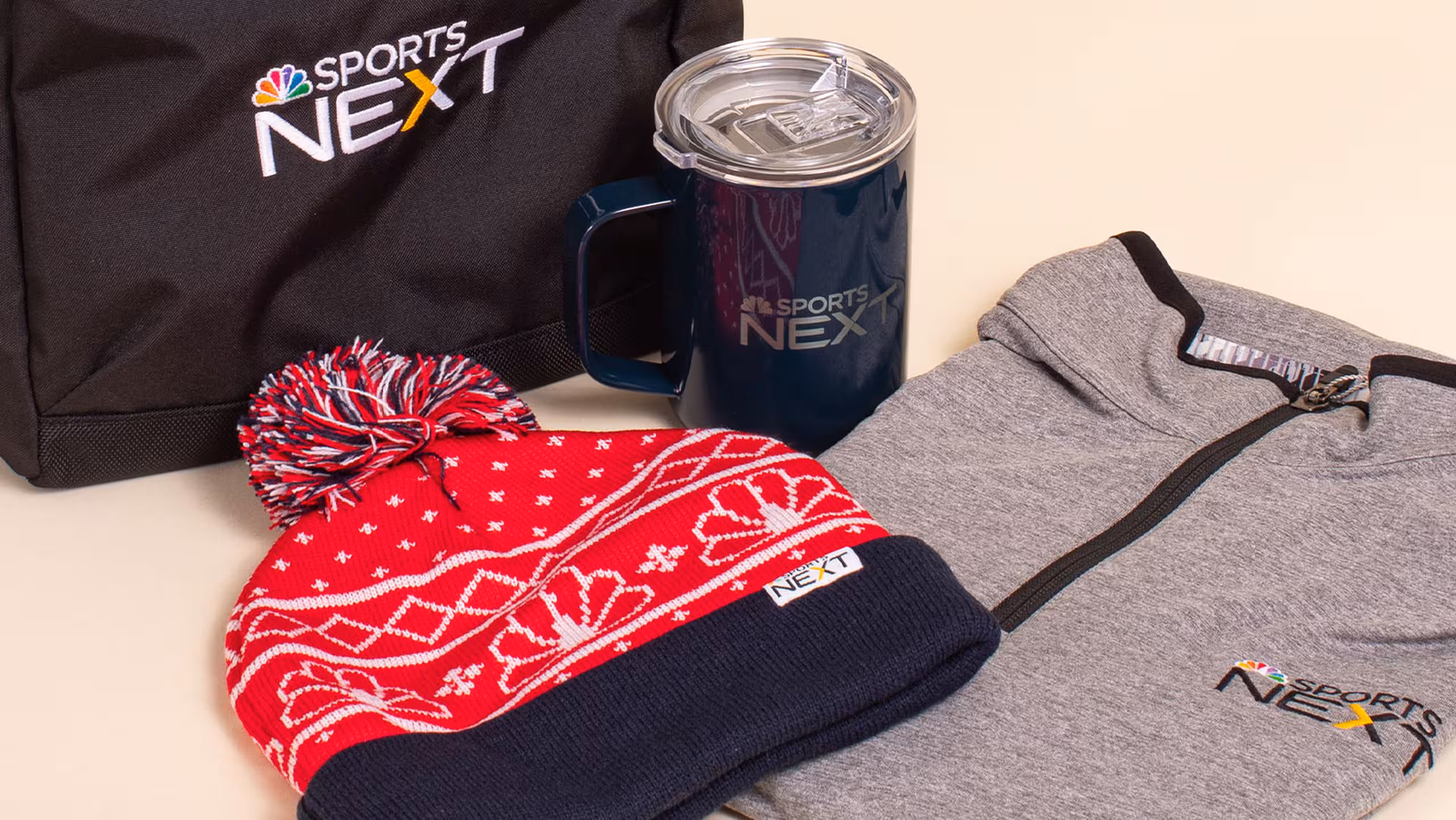 collection of gifts, beanie hat, quarter-zip sweatshirt, cup, and cooler bag