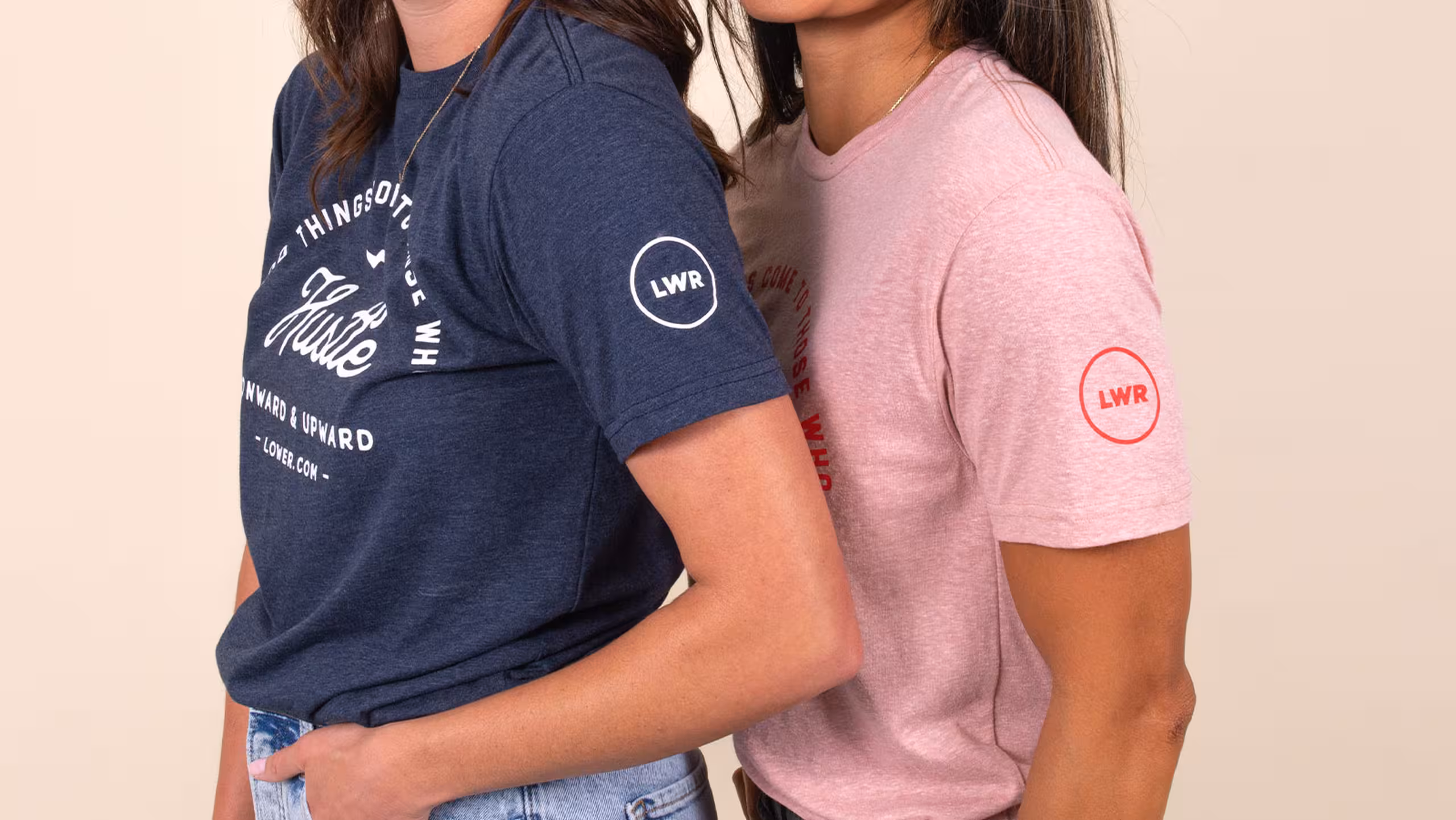 Two women with their left side facing the camera. One wearing a navy t-shirt and a pink t-shirt.