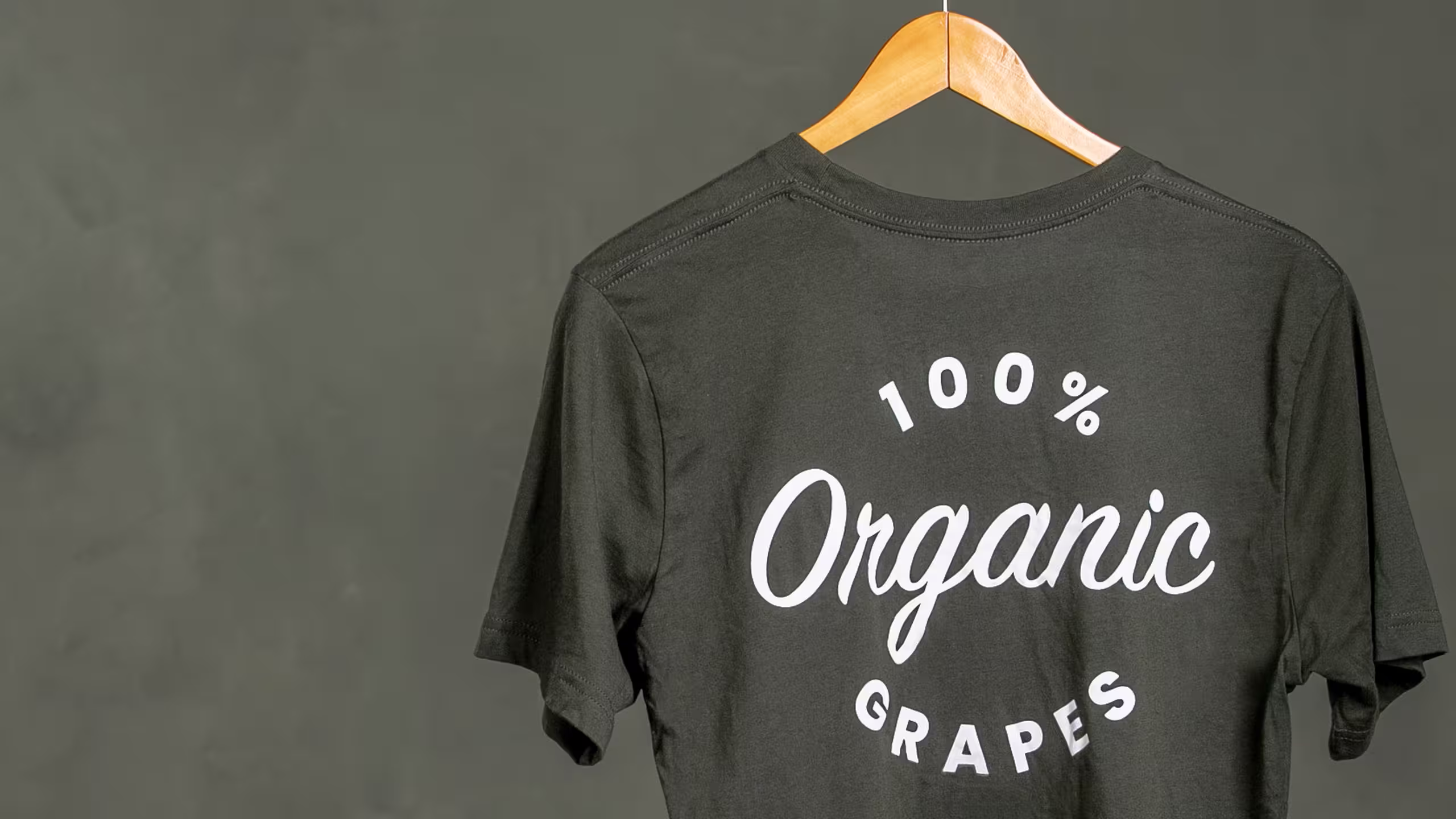 dark olive green t-shirt with the words 100 percent organic grapes hanging on a hanger